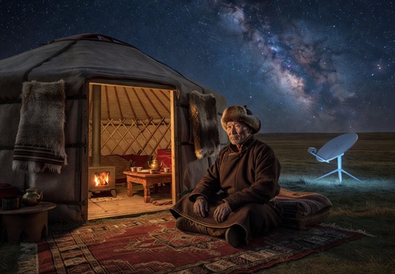 A Mongolian herder sitting inside a traditional ger tent at night, a sleek white satellite internet terminal visible outside the open doorway against a breathtaking starry sky, warm amber light glowing from inside contrasting with the cold blue light of the terminal, photorealistic, cinematic wide shot, sense of two worlds meeting, vast steppe landscape stretching to the horizon